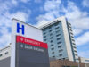 The outside of a hospital (building with an H sign and directions to different areas)